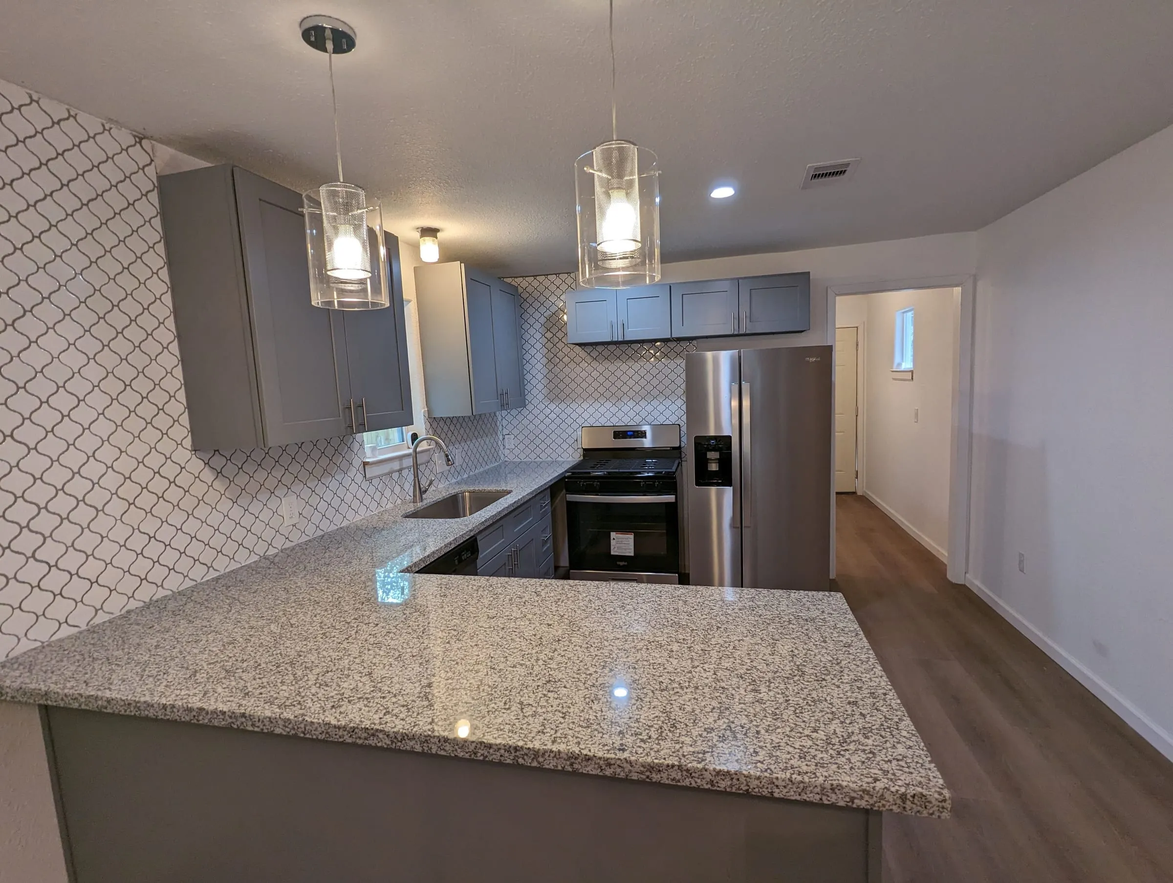 Kitchen with gray cabinets, a granite island, pendant lights, and stainless appliances